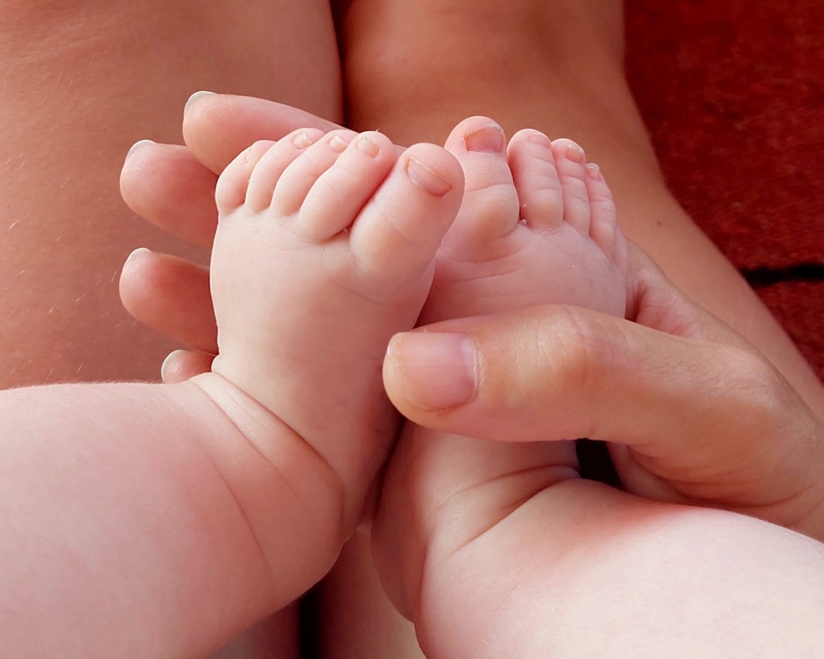 Massage bébé : mains d'un parent enveloppant délicatement les pieds de son bébé